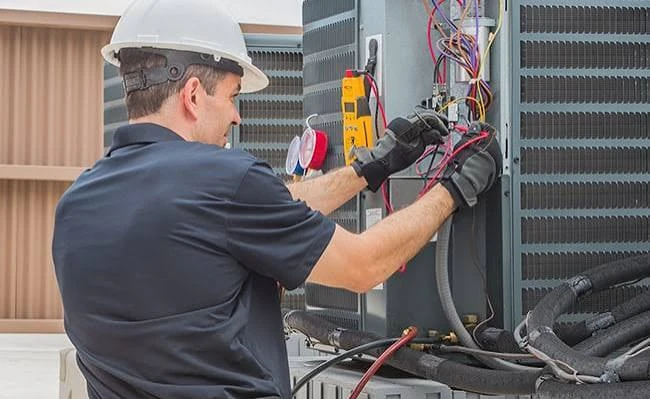 Technician checking electrical components inside outdoor HVAC equipment