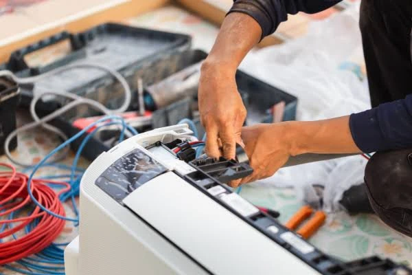 Technician working on an open indoor air-conditioning unit with tools nearby
